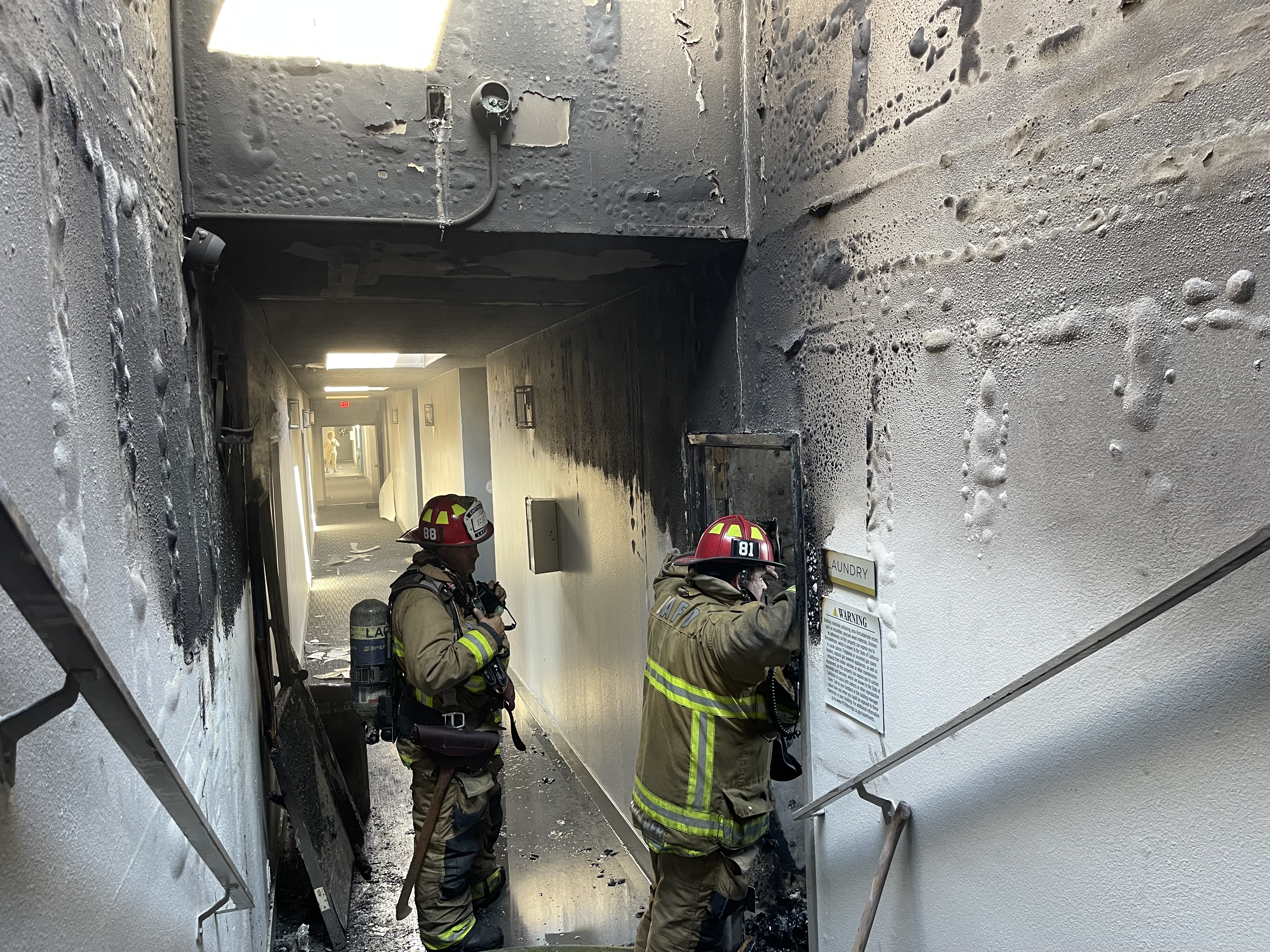 Firefighters standing in burned hallway of apartment building.
