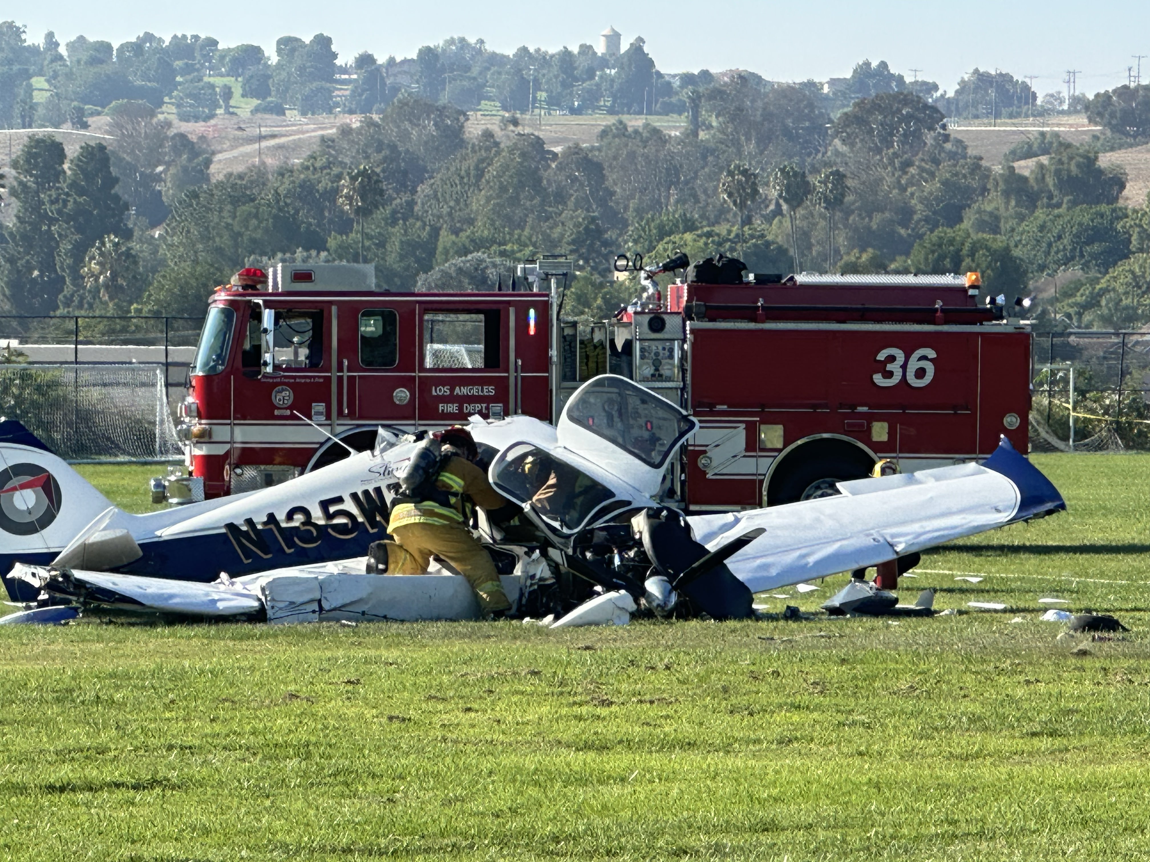 small plane crashed on grass with fire engine in the background