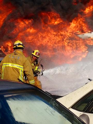 Two firefighters in front of a wall of flames.