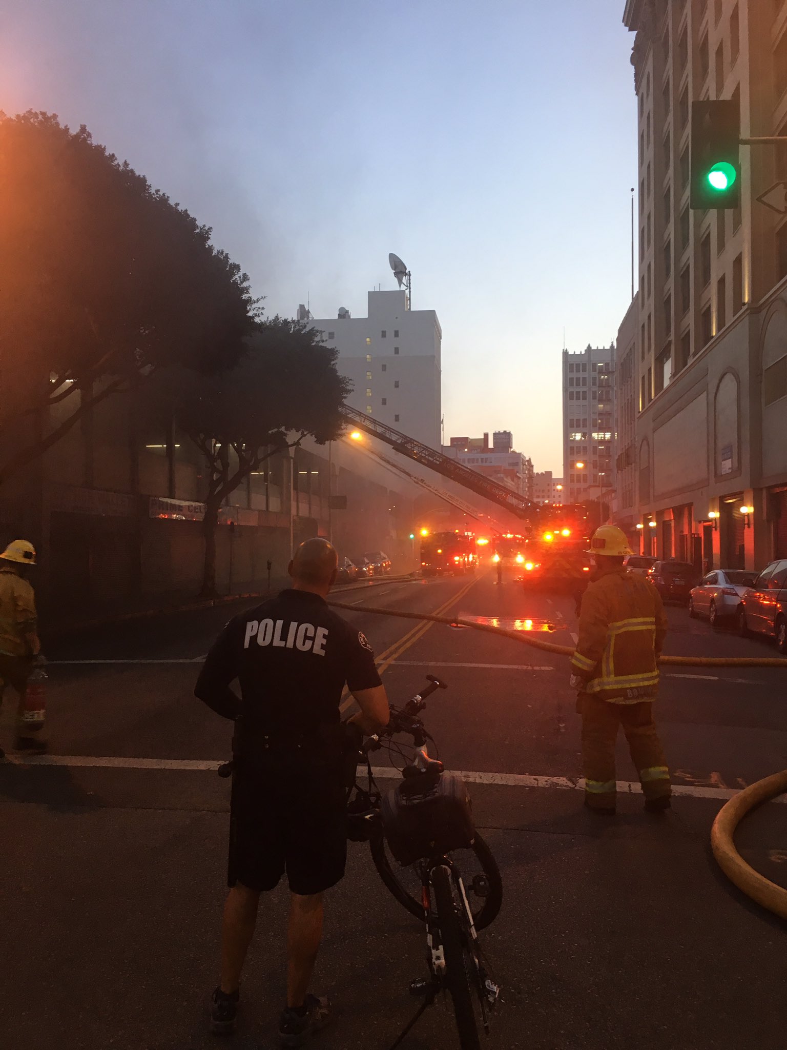 Fire and police seen with building in background, smoke emanating 