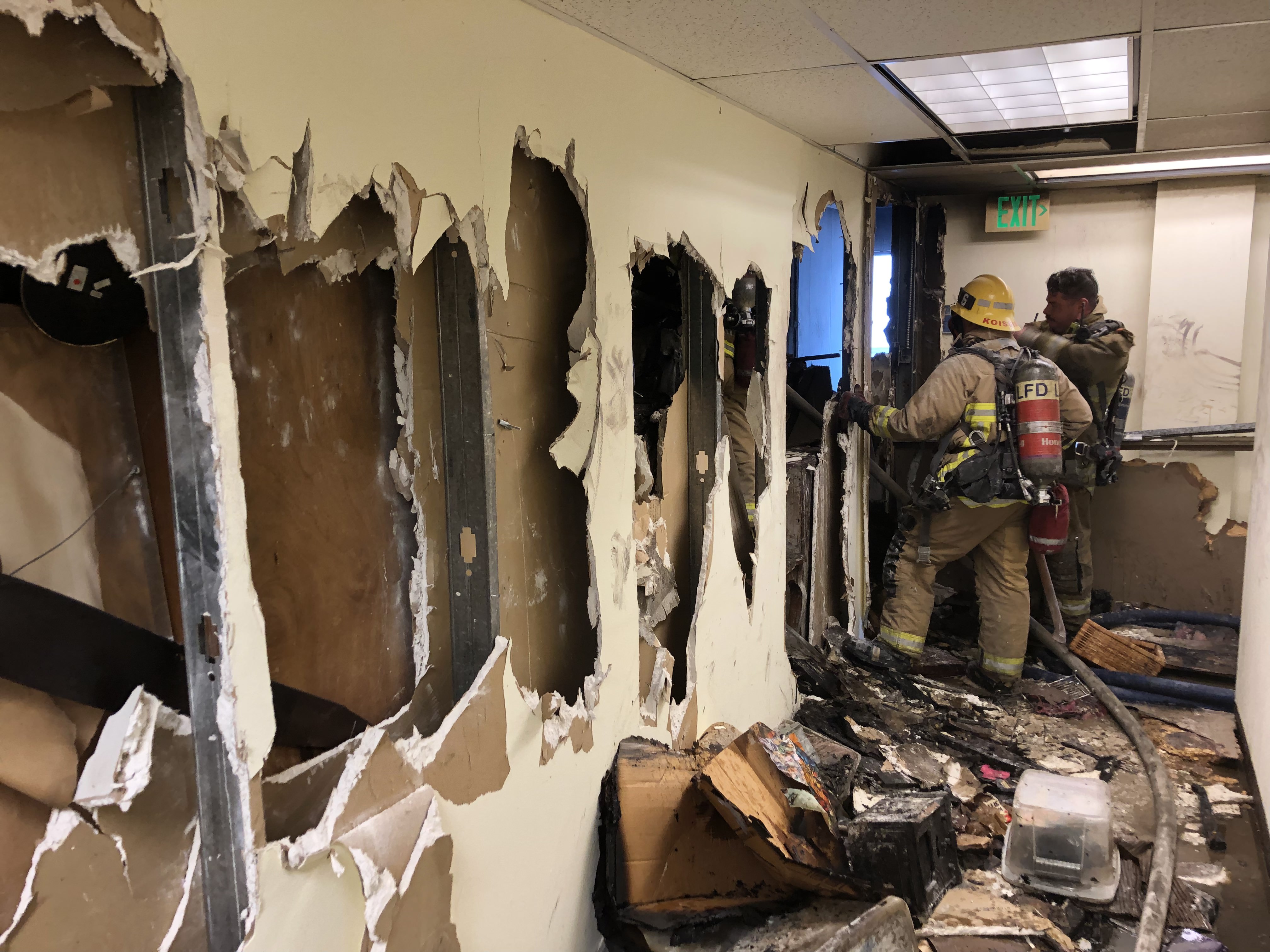 Numerous holes in dry wall seen down the hallway with firefighters