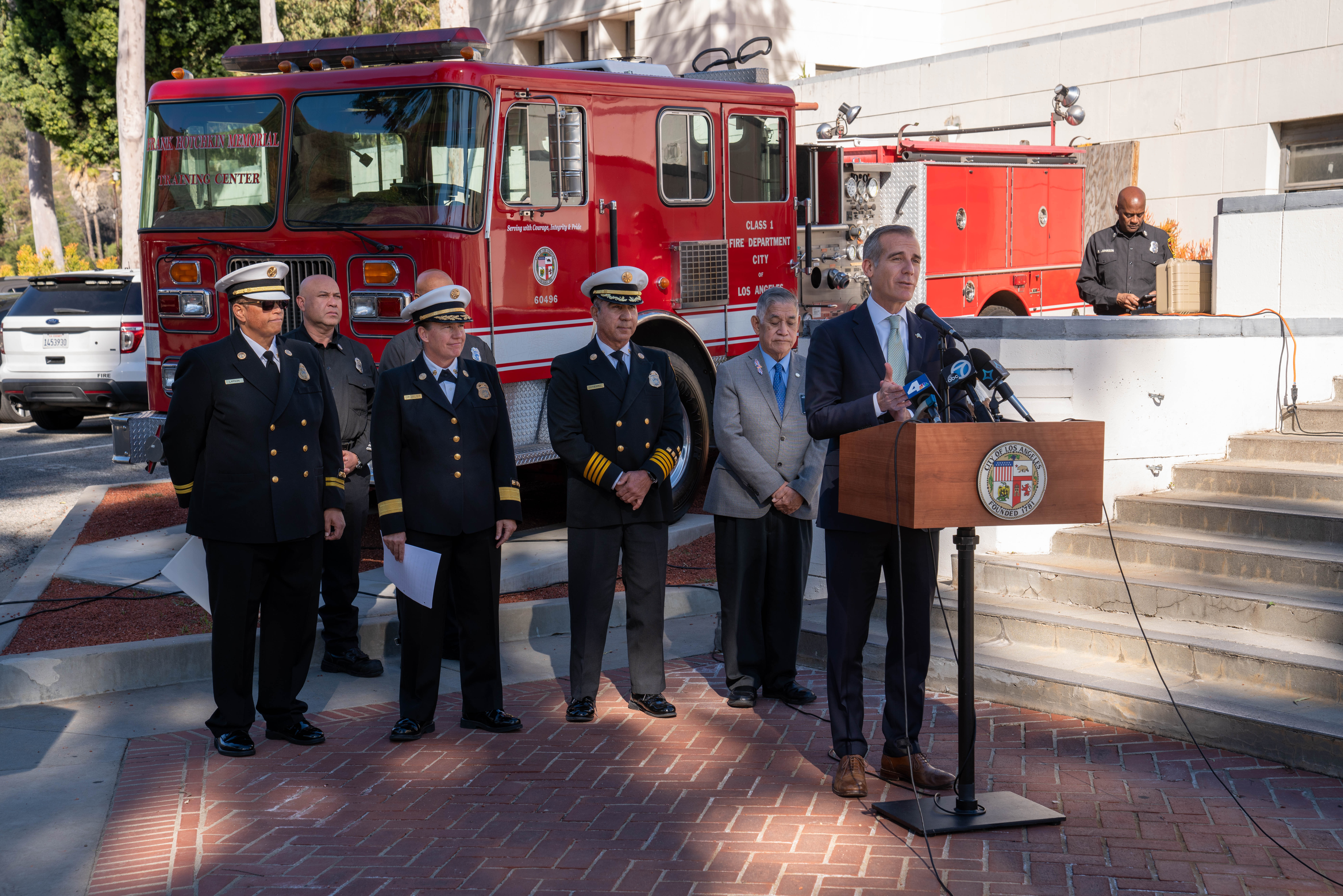 Mayor Garcetti speaking at a lectern with a fire engine and several fire chiefs behind him.