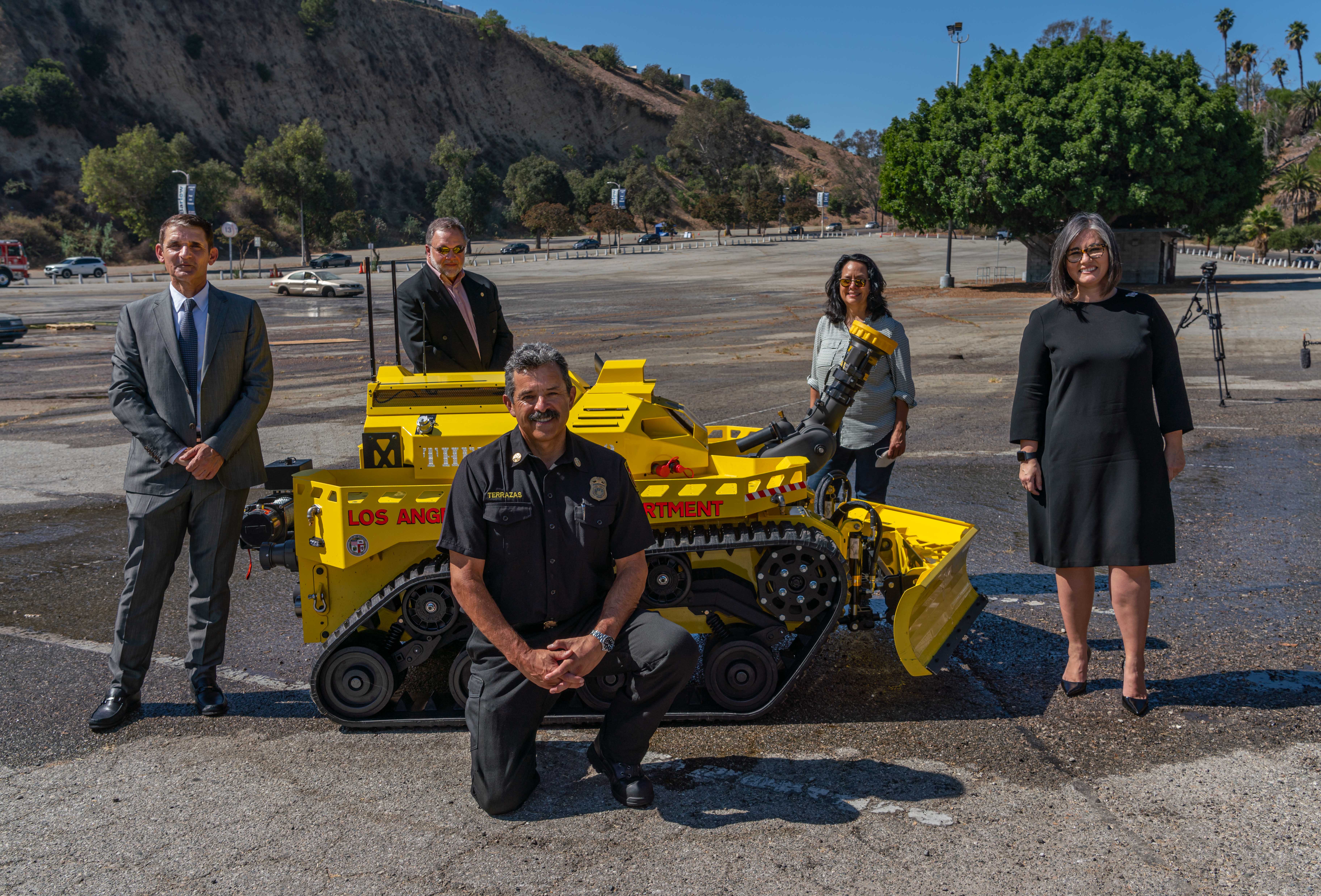 Fire Chief and city officials standing with the yellow, robotic firefighting vehicle - a compact tracked vehicle